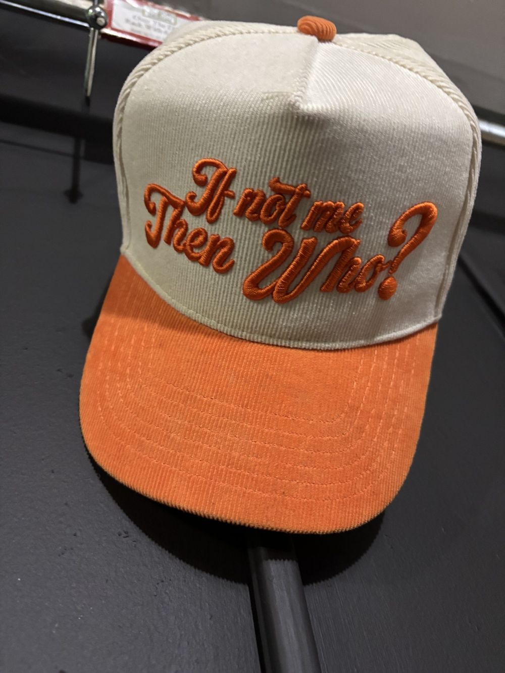 Cream and orange corduroy If Not Me Then Who hat on display
